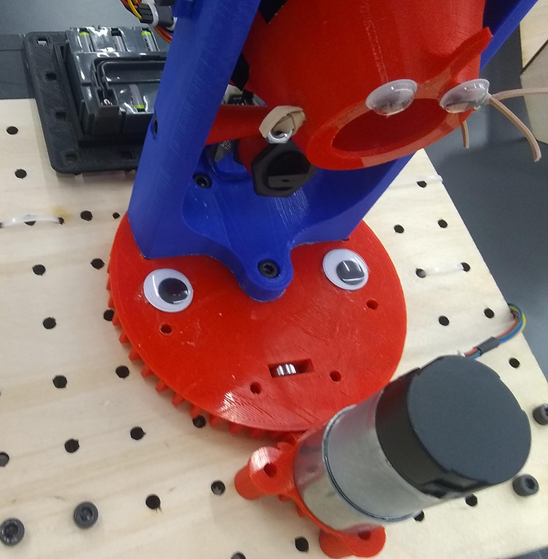 Googly eyes on a 3-D printed plastic part. A small slot looks like a mouth and a bolt looks like a nose.