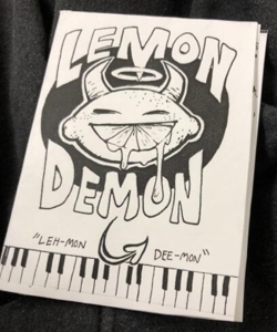 Lemon Demon minizine cover. Has the band name and a lemon with demon horns and a halo. A slice out of the lemon serves as its grin.