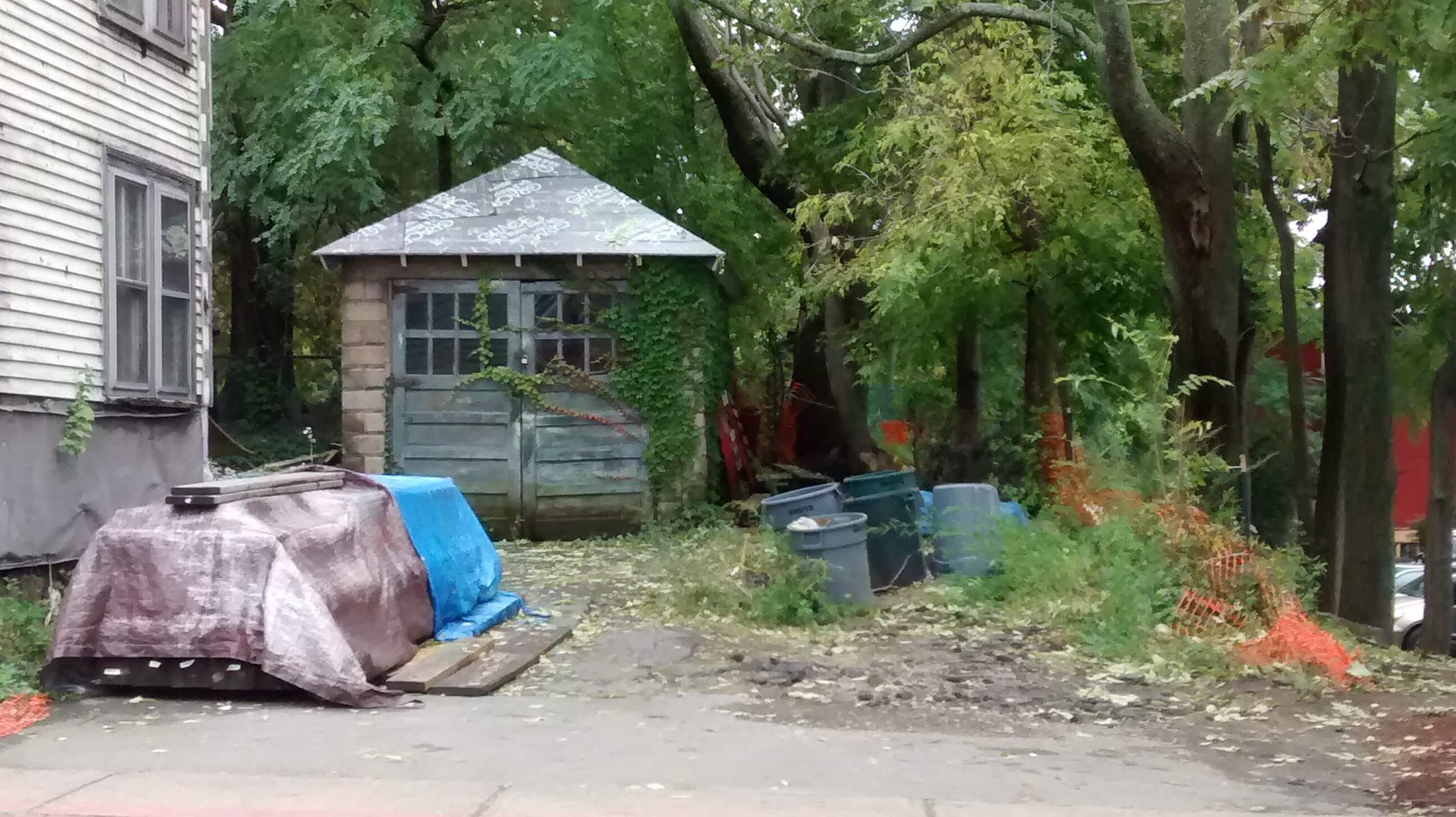 A shed with an overturned boat and a blue tarp over it.