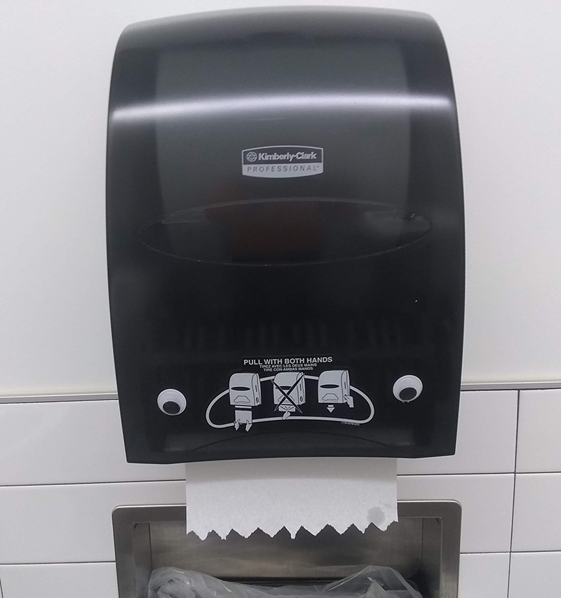 Googly eyes on a paper towel dispenser. The paper towel comes out like a tongue.