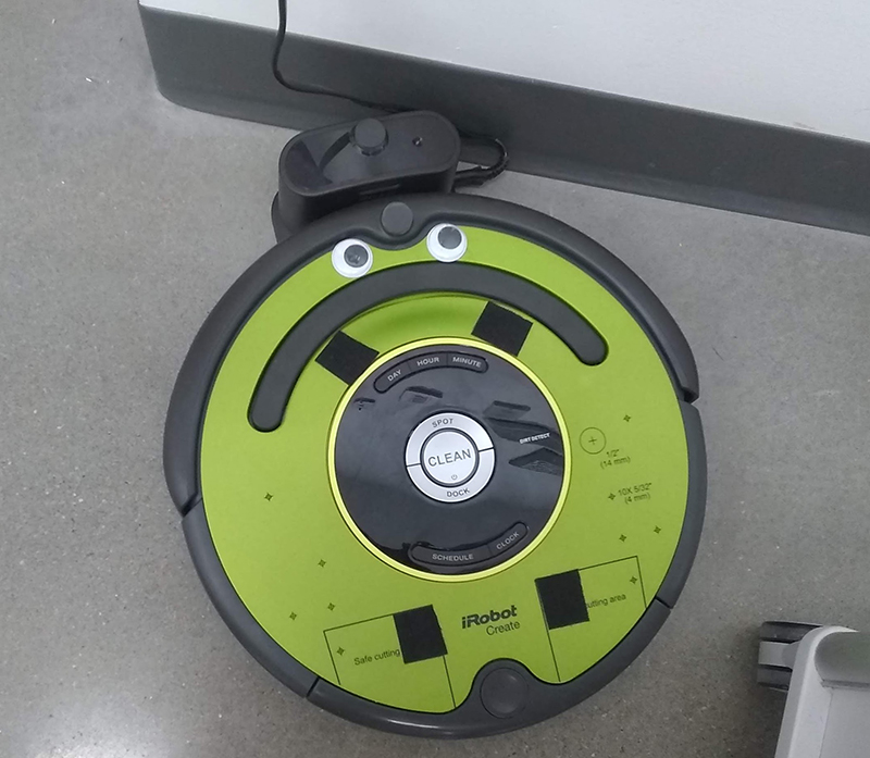 Googly eyes on a roomba. A natural line on the roomba looks like a large, sad frown.
