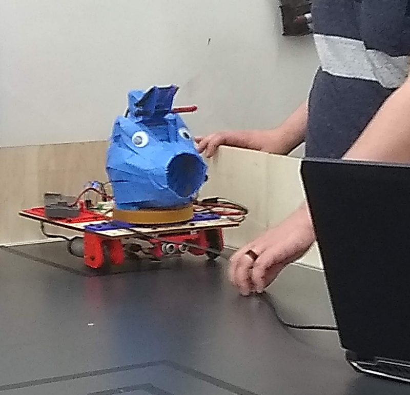 Googly eyes on a cone covered with tape on a wheeled robot. It looks shocked and derpy.
