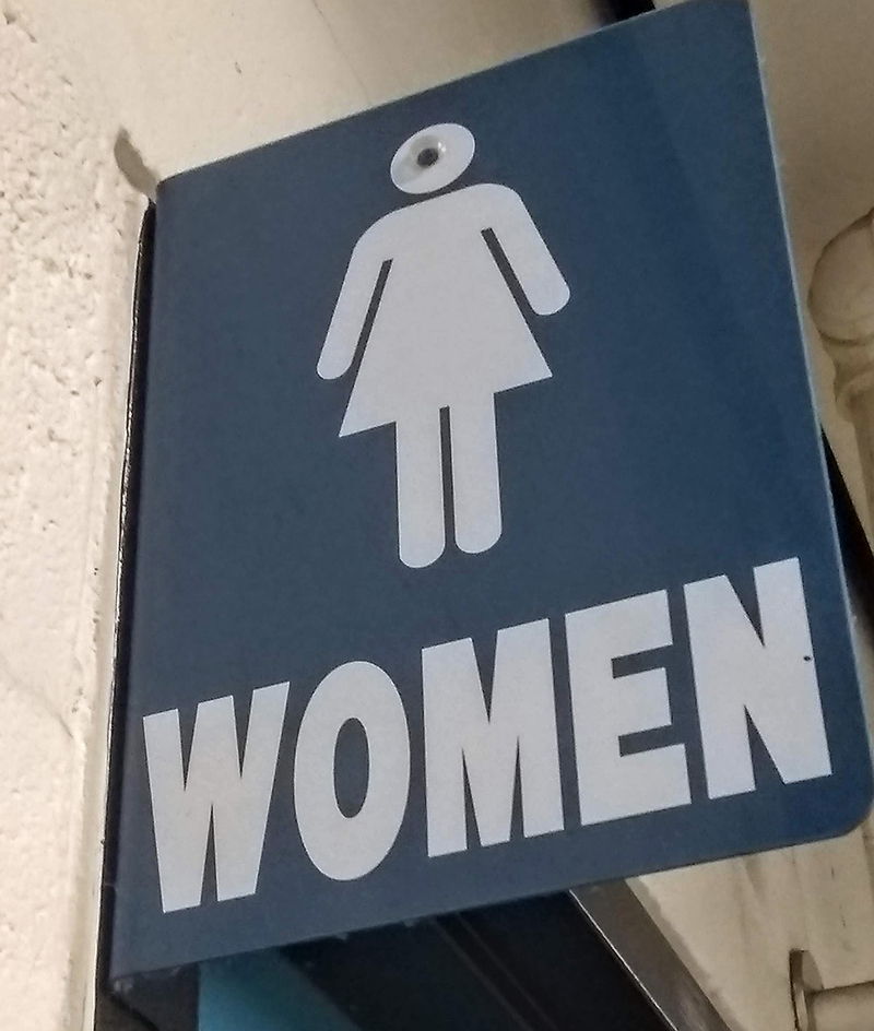A single googly eye on a women's restroom sign. The generic female figure looks like a cyclops.