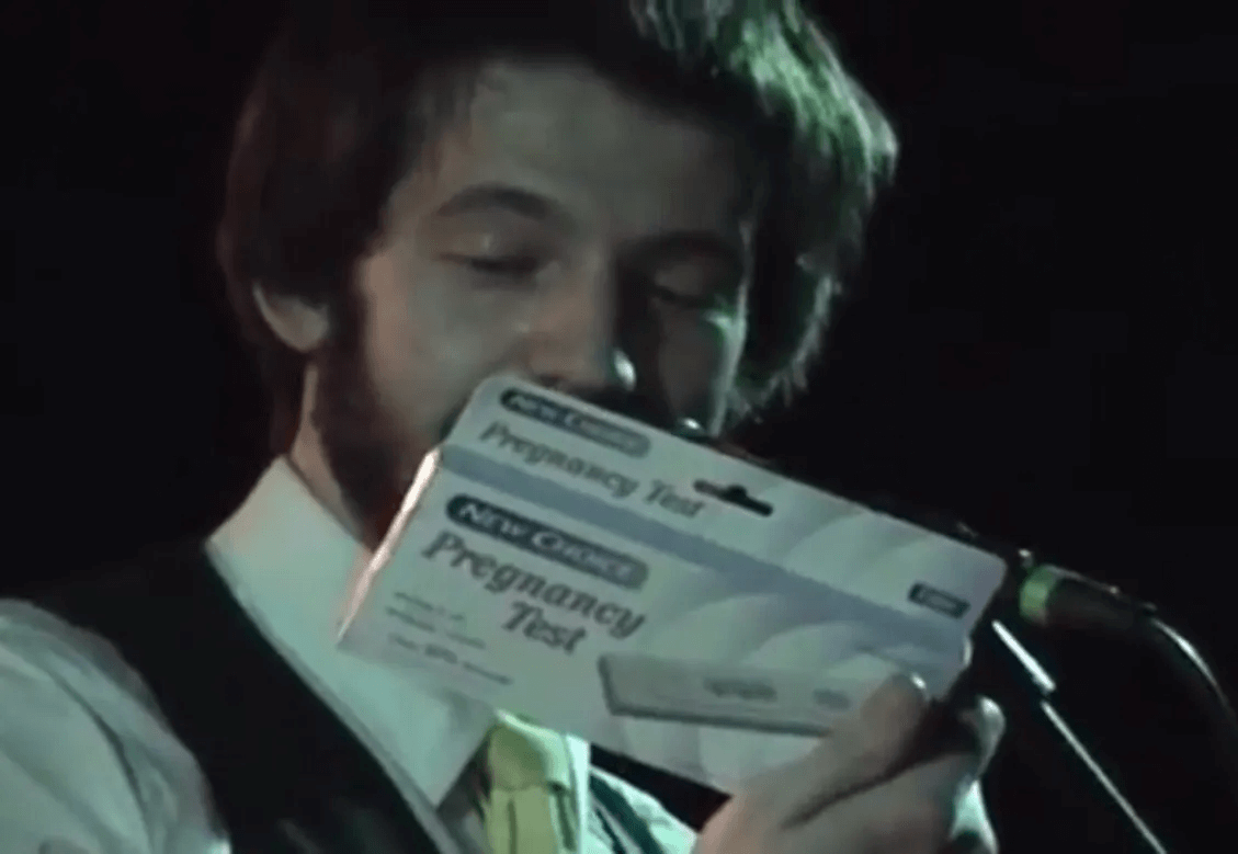 Rob Cantor onstage, holding a pregnancy test